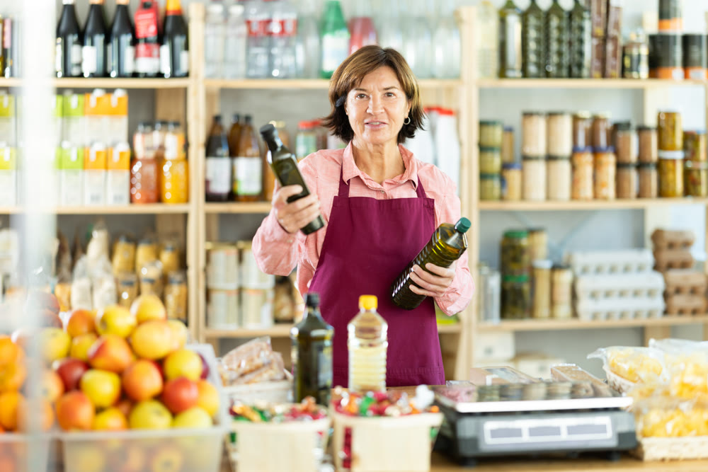 Experienced female salesperson offers choice of buying bottle of vegetable oil or olive oil in grocery store