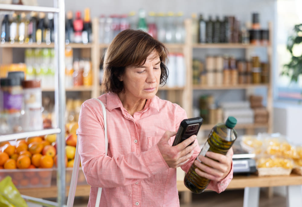 Female buyer checks suitability - scans QR code on olive oil label in grocery store