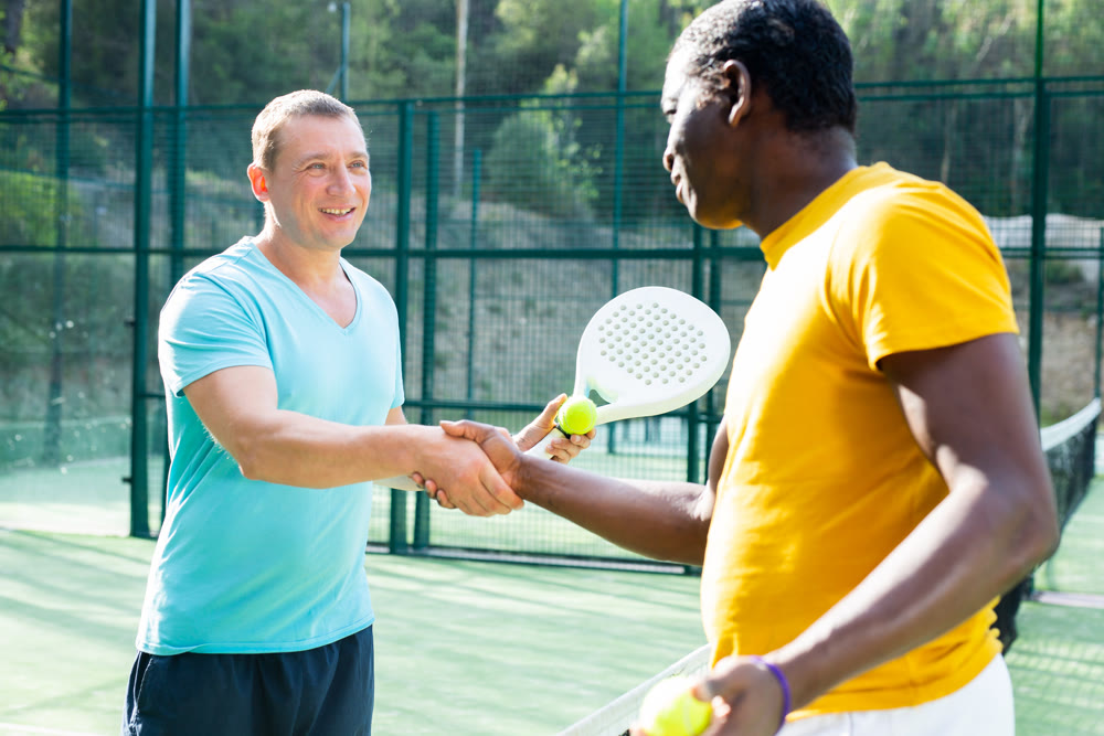 Two men padel tennis players shake hands amicably