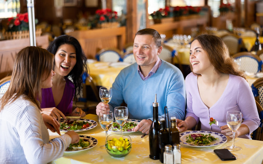 Adult men and women having friendly meeting at dinner in restaurant