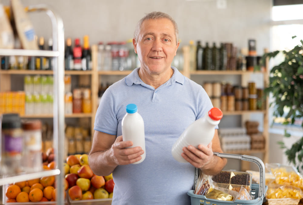 Mature man hold white plastic bottles and choose consider milk in store