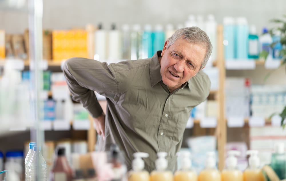 Older man experiencing sharp back pain while shopping in pharmacy