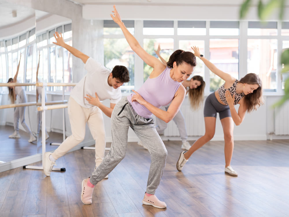 Cheerful young girl and multinational people training synchronous group choreography in dance studio