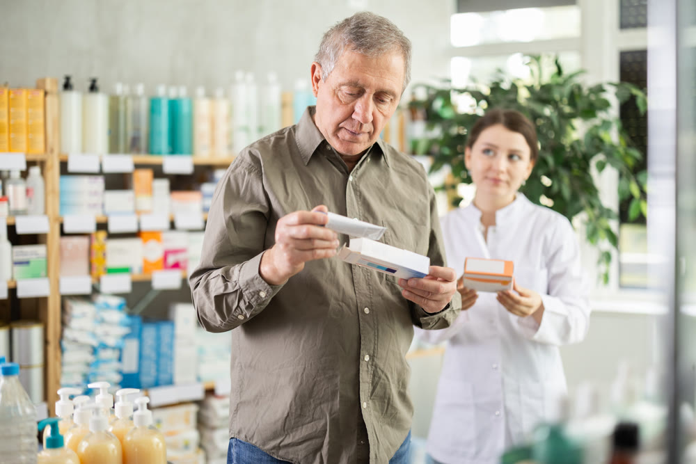 Senior man buys antibacterial ointment at drug store, girl pharmacist in background