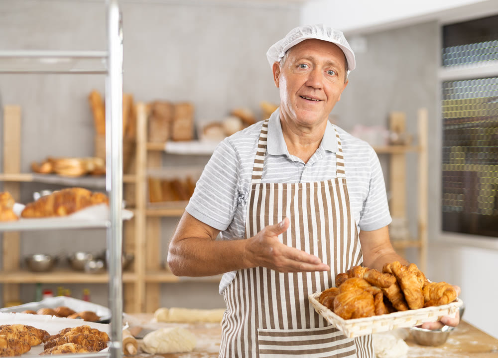 Bakery mature man employee holds basket of ready-made croissants.