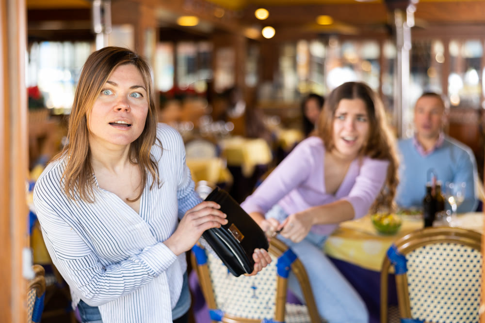 Female thief stealing handbag of frightened woman in restaurant