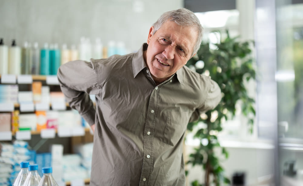Older man experiencing sharp back pain while shopping in pharmacy