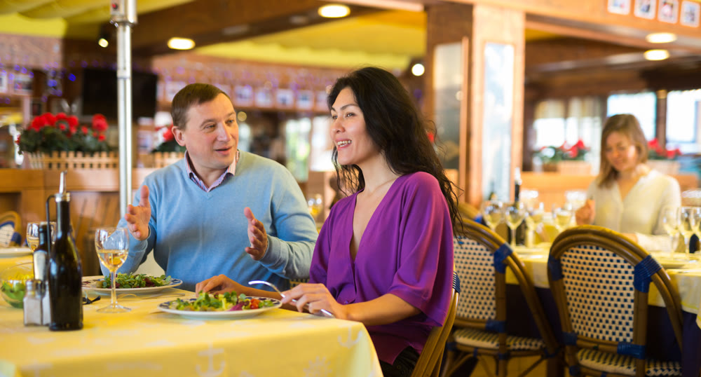 Cheerful adult interracial couple having dinner in restaurant
