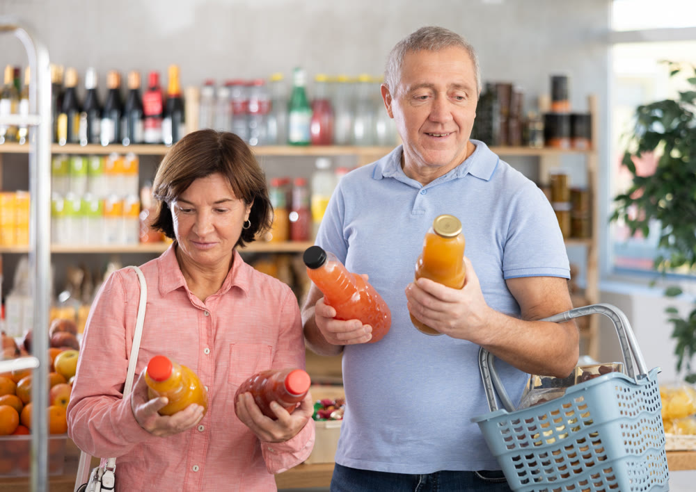 Couple elderly man and woman choosing juices in grocery store