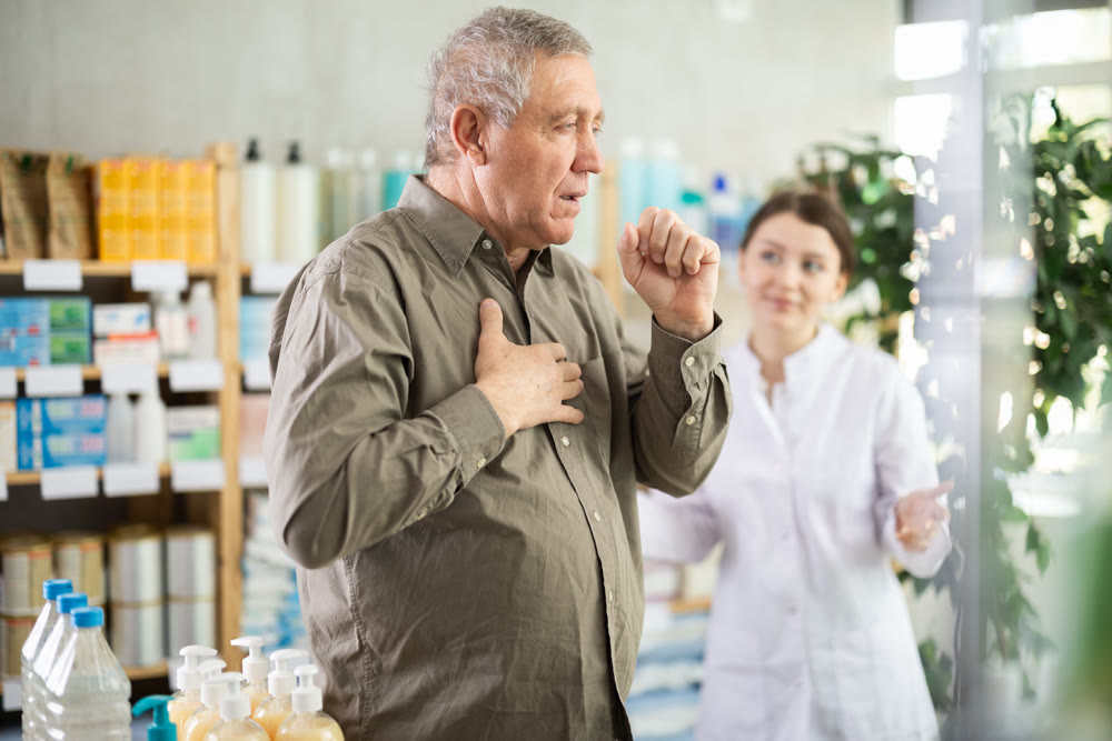 Elderly man with sore throat is looking for medicine in pharmacy. Female pharmacist is helping him