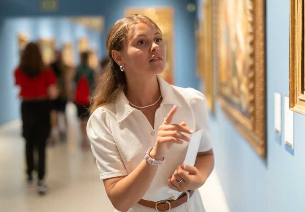 Portrait of young girl visitor with paper guide at the exhibition of paintings in museum