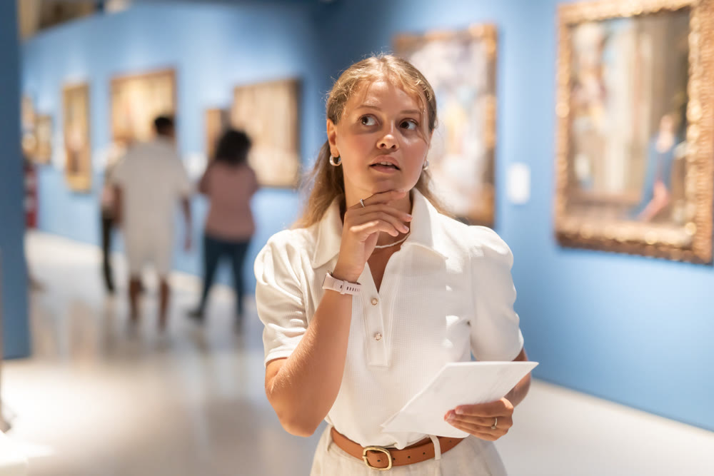 Young girl holding an information booklet looks at paintings in an art exhibition in museum