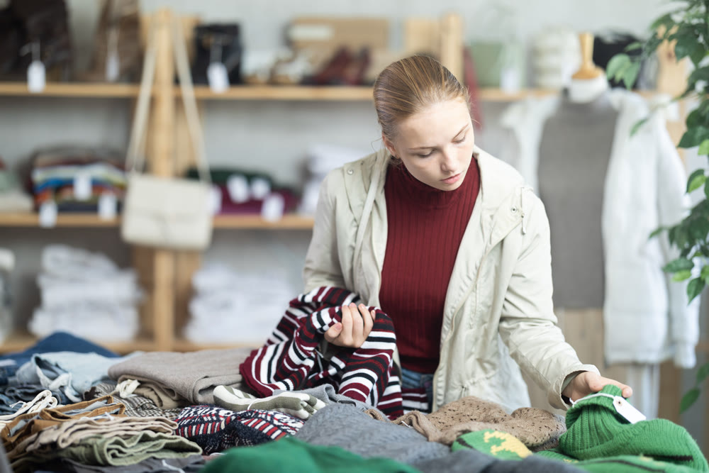Selective teen girl choosing sweater in clothing store