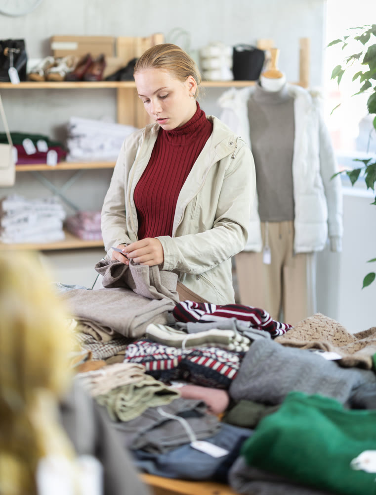 While shopping, teen girl browsing goods items and choose elect trousers in store