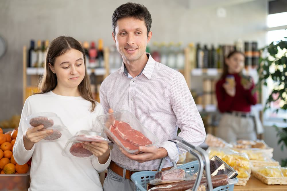 Father and daughter choose raw cooled beef entrecote and hamburger cutlet in shop