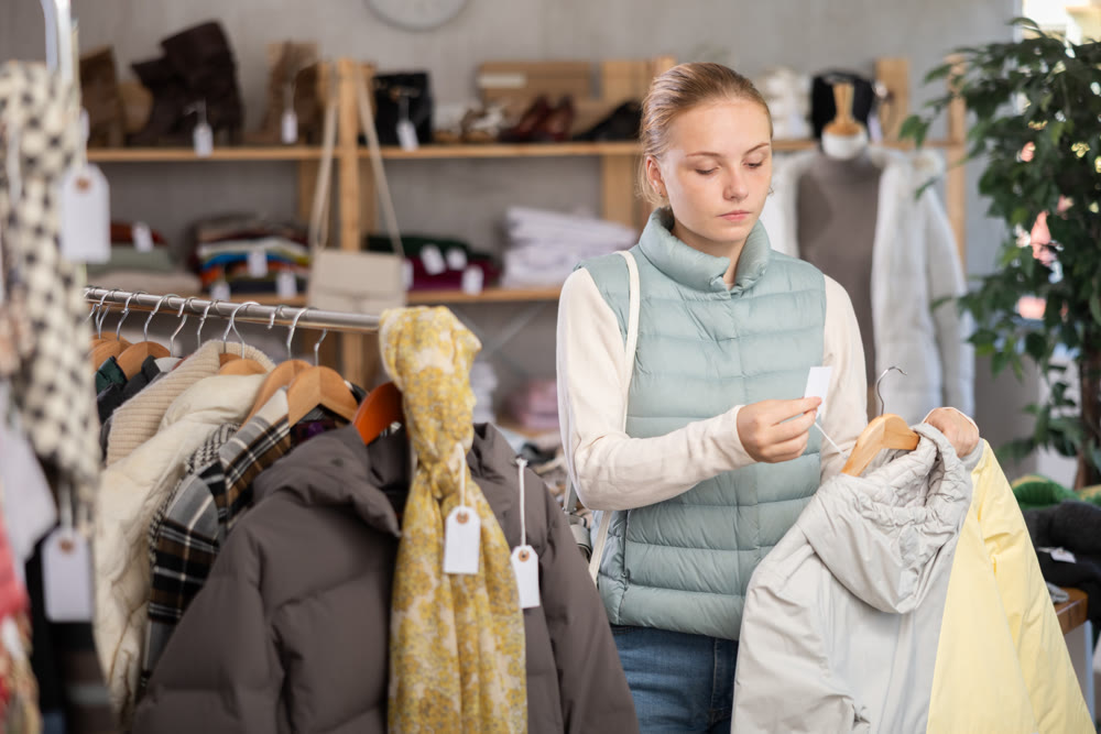 Attentive teenage girl choosing lightweight jacket in clothing store