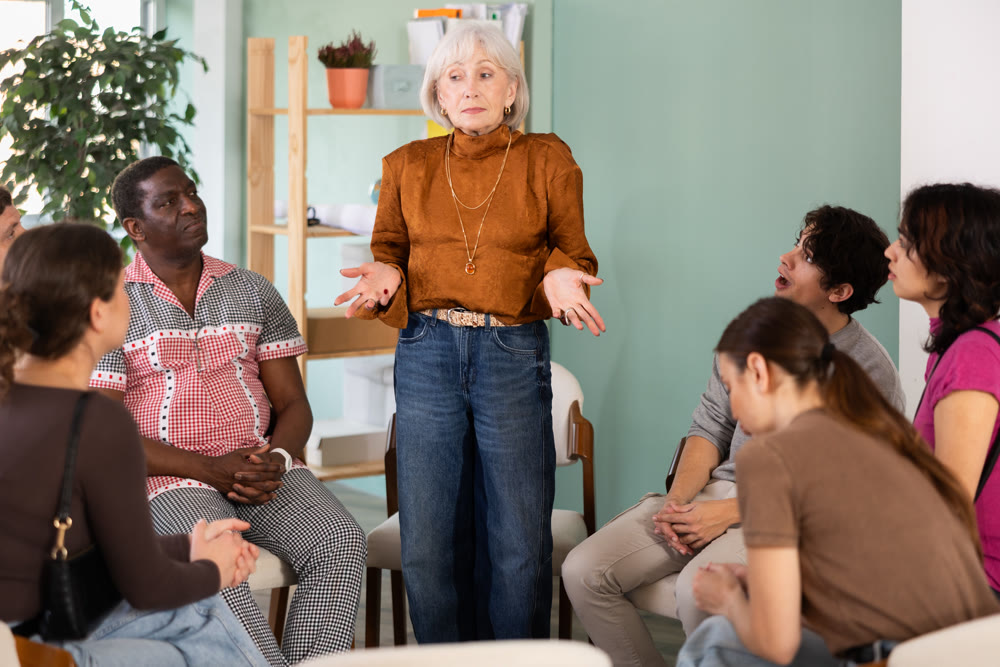 Elderly woman communicating with a people in a circle on the background of an office
