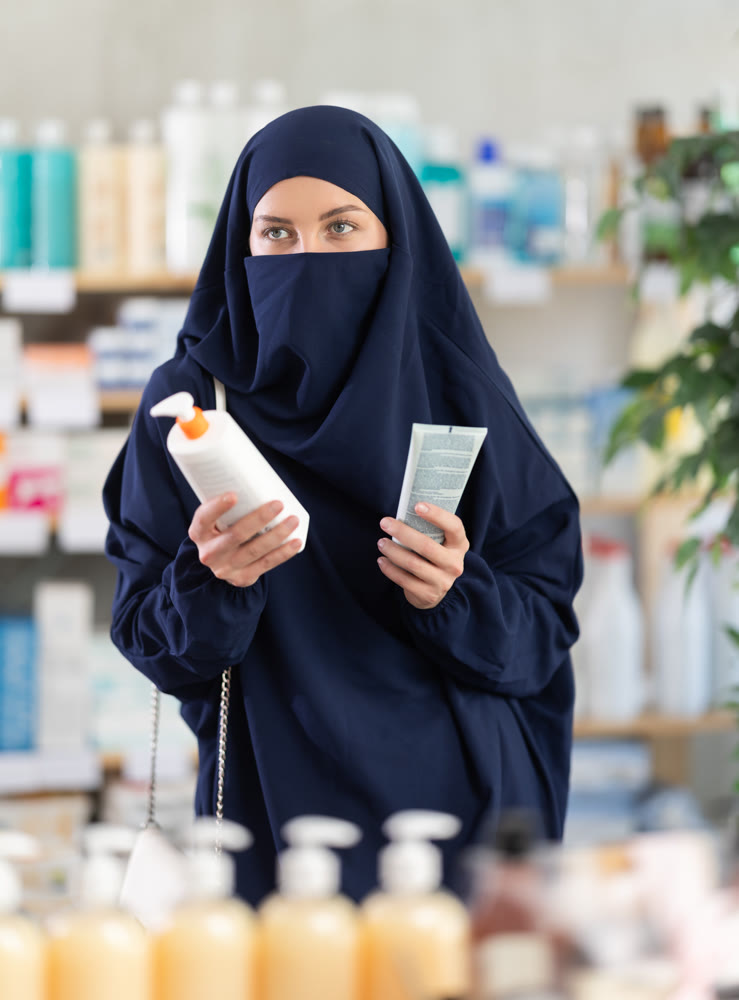 Young Muslim woman choosing cream in drugstore