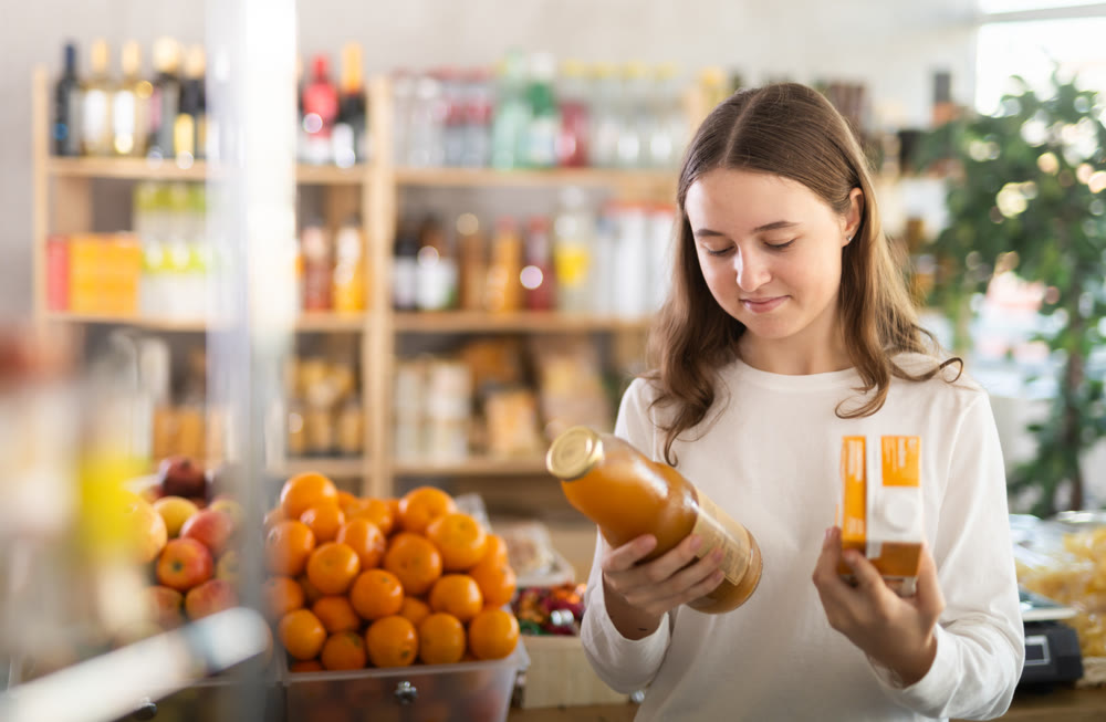 Teenage girl choosing peach juices at grocery store