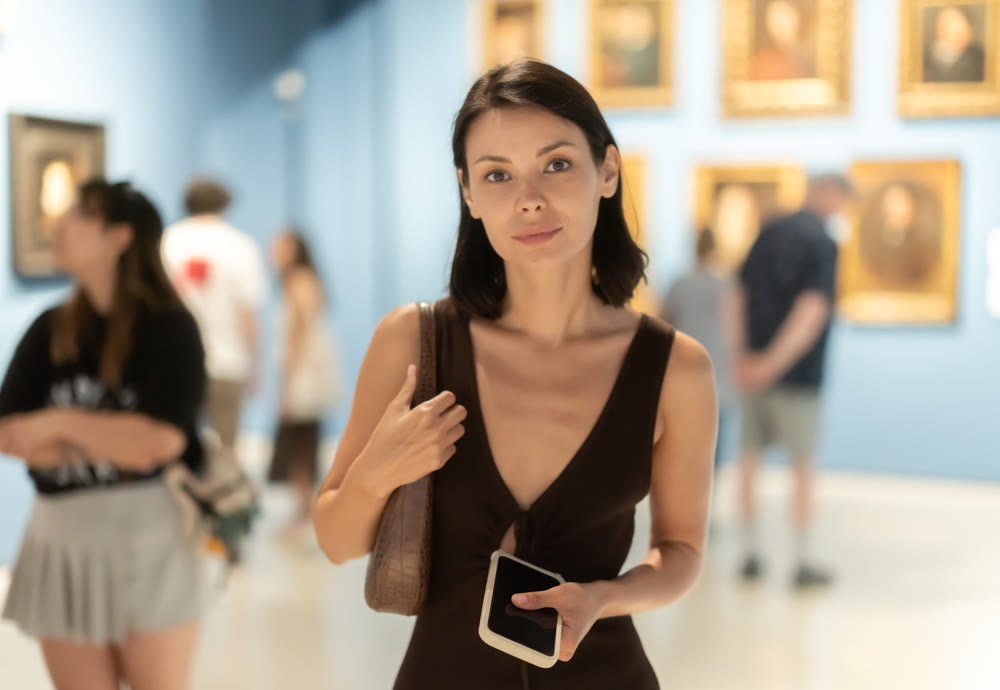 Woman with phone in hands in museum hall, view painting exhibition