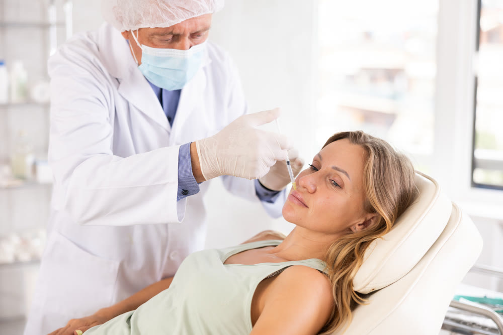 Male doctor gives injection and performs procedure of lip augmentation of female patient in clinic.