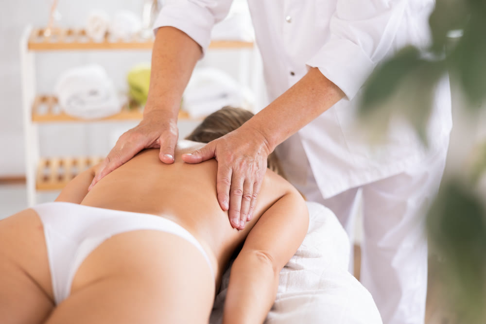 Hands of old masseur conducting back massage for woman client