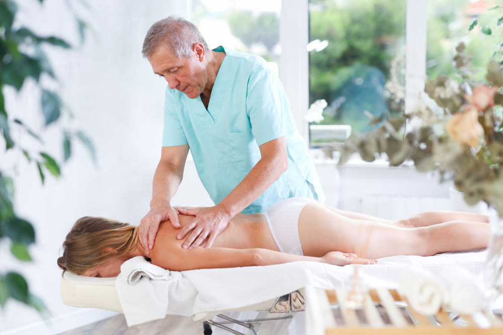 Skilled old masseur conducting back massage for woman client