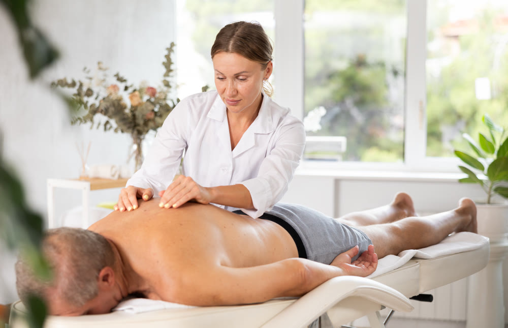 Skilled middle-aged masseuse conducting back massage for man client