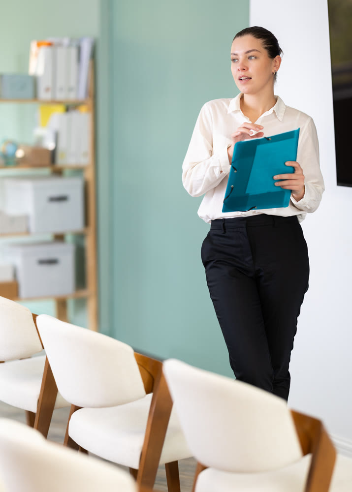 Female coach with folder with papers standing near blackboard in classroom