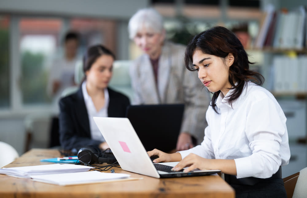 Young woman works on laptop with female colleagues