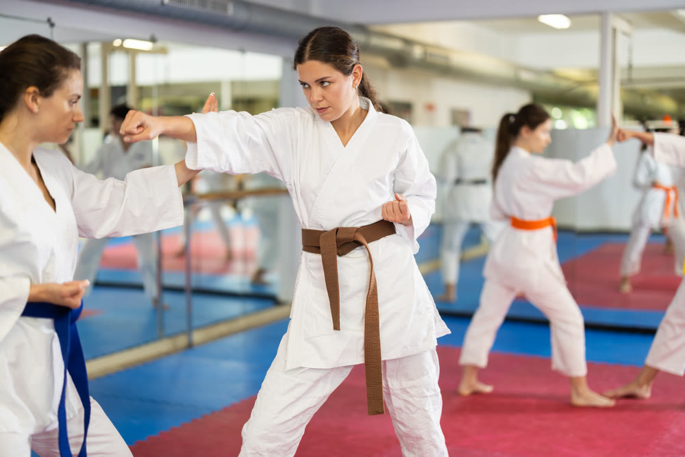 Womens practicing new karate moves in pairs in class with trainer