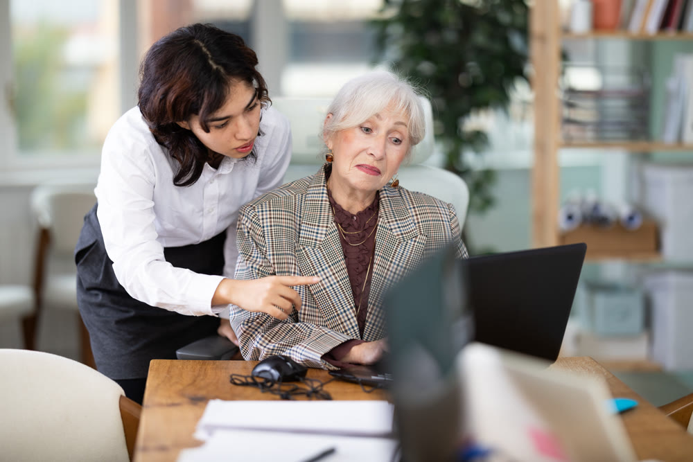 Young girl helping mature colleague with tasks on laptop