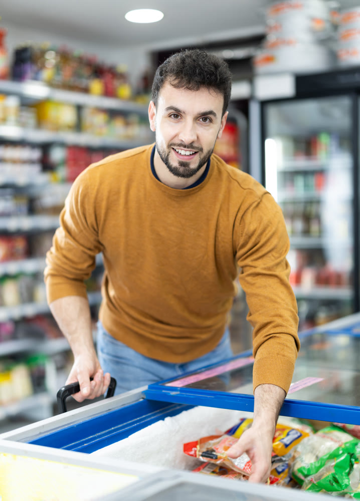 Man choosing frozen food in supermarket. Man purchasing goods in store