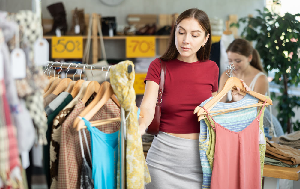 Young girl elect something summer clothing in store. Female client choosing something in background
