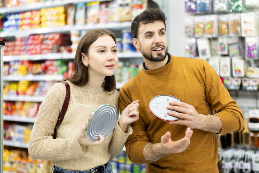 Couple of shoppers are choosing canned fish in food store