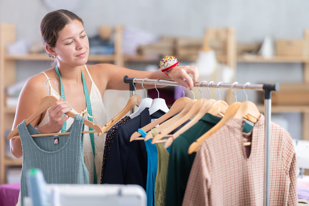 Young dressmaker taking finished dress from rack