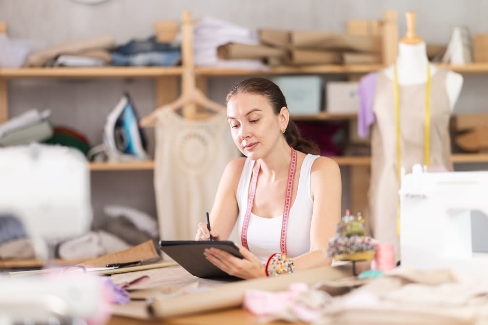 Young female dressmaker drawing on tablet in sewing workshop
