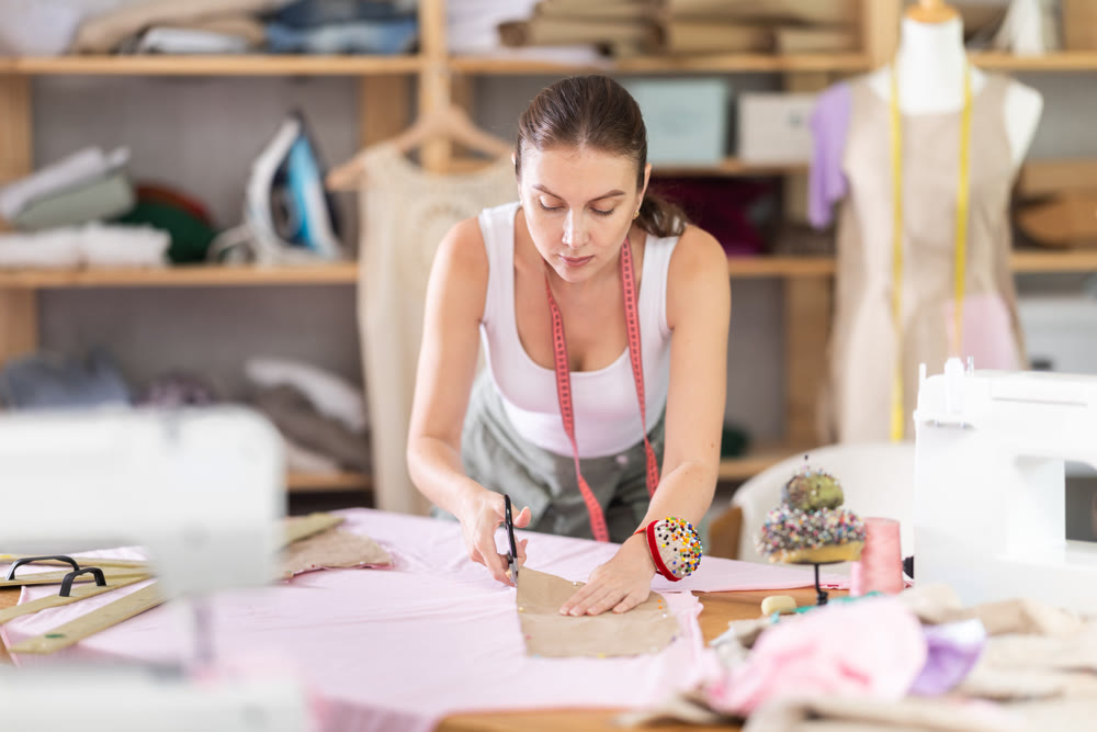 Young female dressmaker cutting textile in sewing workshop