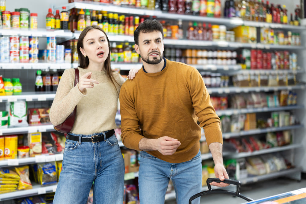 In food store, couple buyer looking for something on shelf of showcase