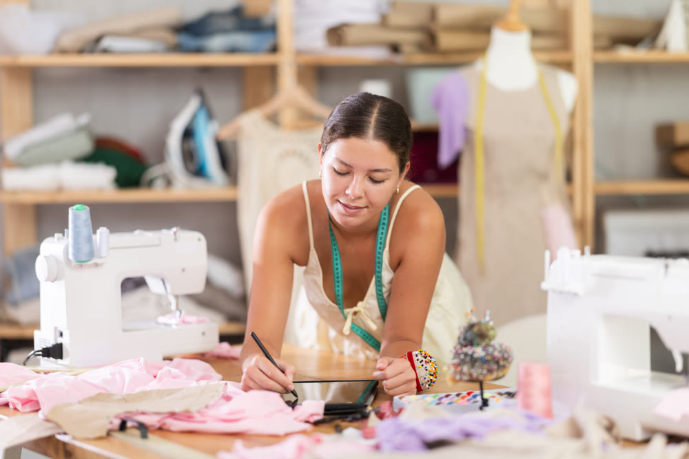 Young female dressmaker drawing on tablet in sewing workshop