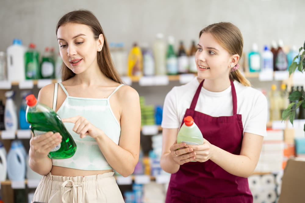 Sales girl offers woman choose dishwashing in household supermarket