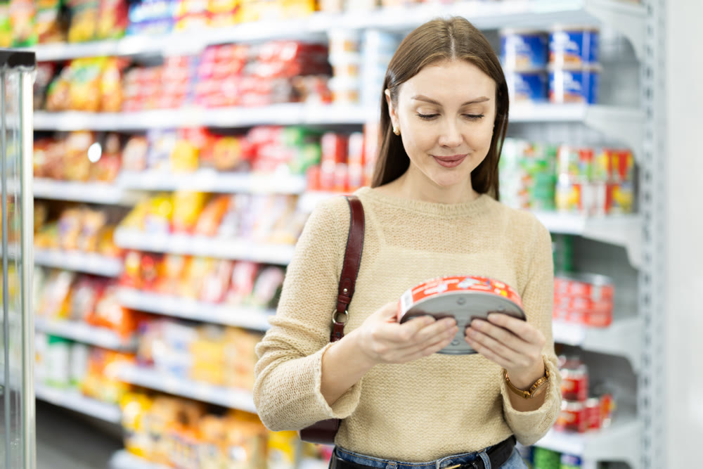 Female shopper are choosing canned fish in food store