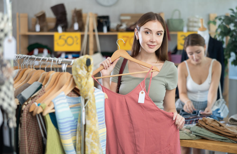 Young girl elect something summer clothing in store. Female client choosing something in background