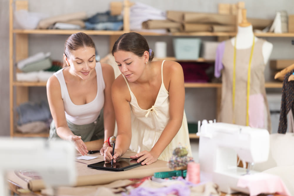 Two young female dressmakers drawing on tablet