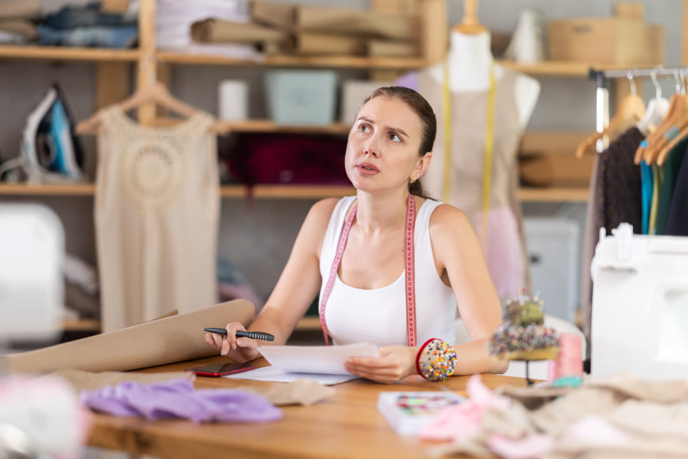 Young tailoress engaged in paperwork in sewing workshop