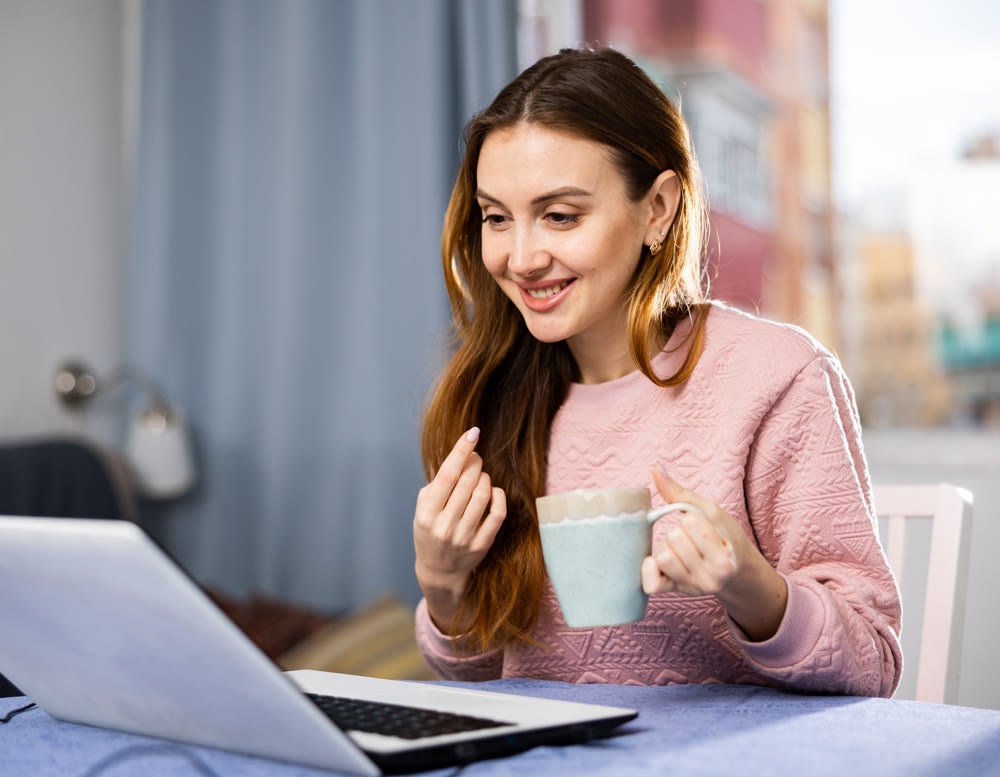 Portrait of young woman sitting at table in living room looking laptop screen