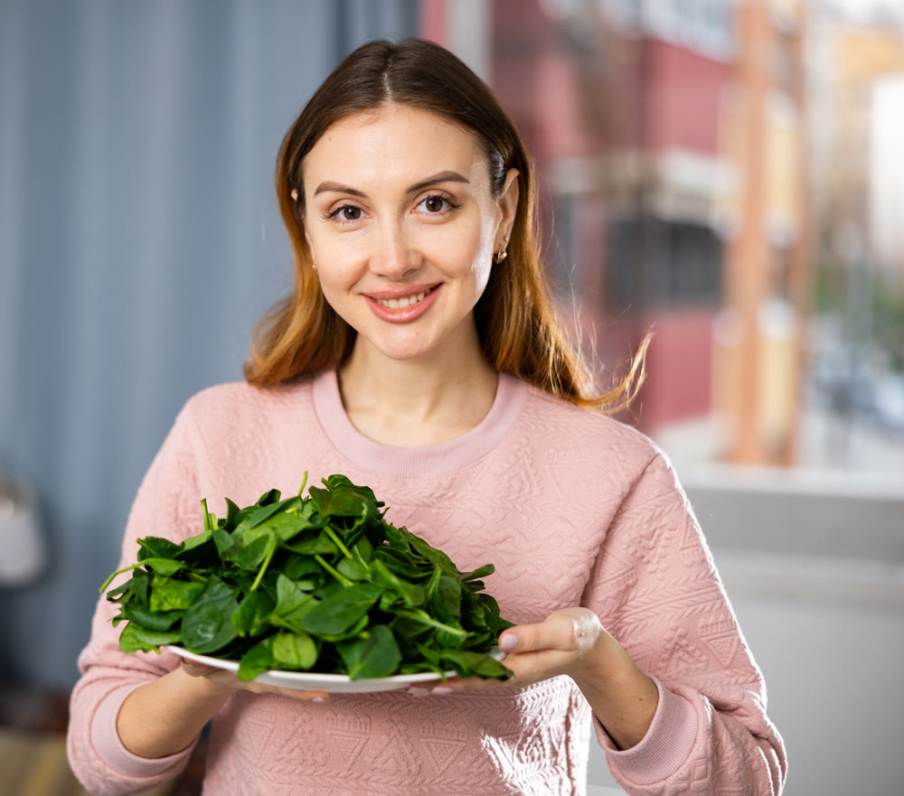 Happy girl making delicious spinach salad closeup