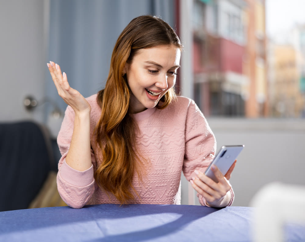 Portrait of pleased joyful woman with smartphone in her hands at the table at home