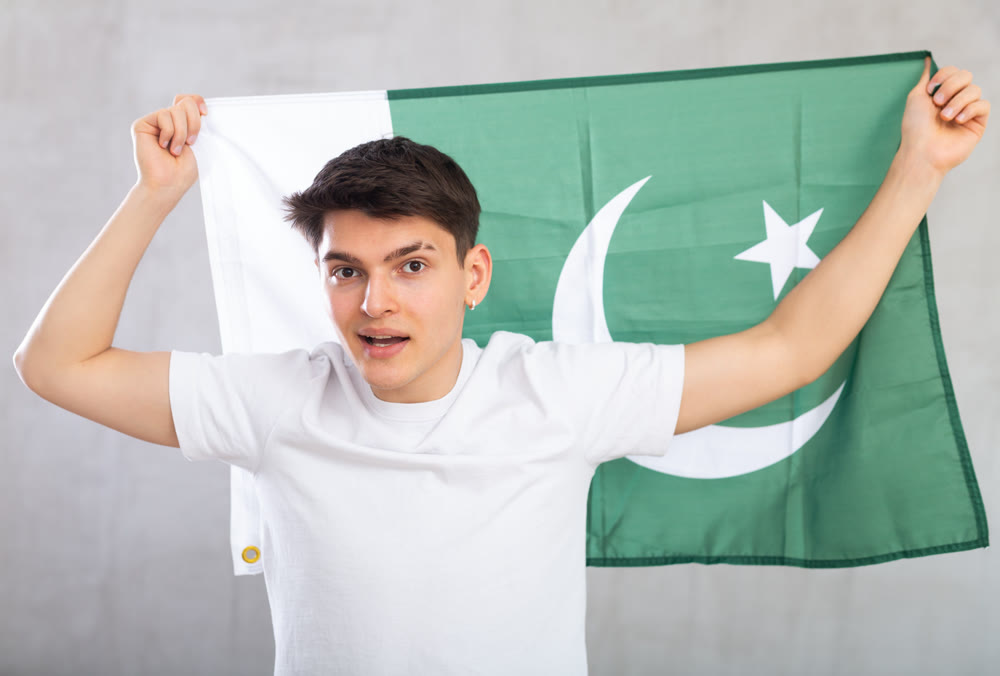 Happy young man holding flag of Pakistan against unicoloured background