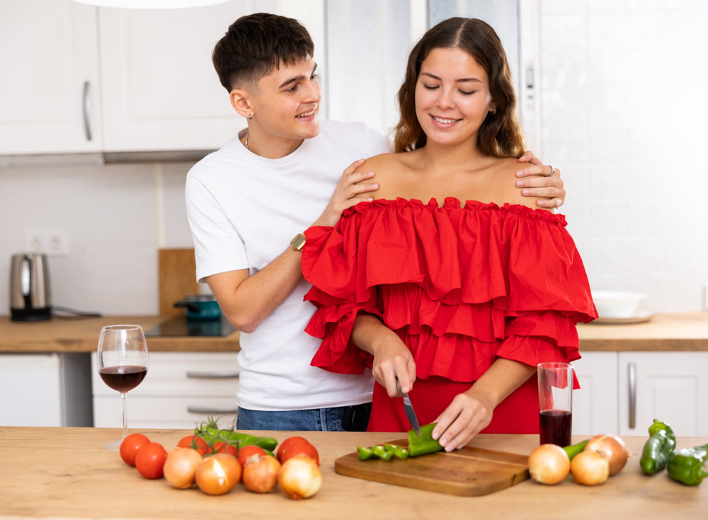 Young happy married couple with glasses of wine preparing a festive dinner